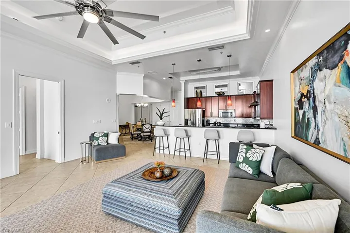 Living room featuring a tray ceiling, light tile patterned floors, ornamental molding, a ceiling fan, and recessed lighting