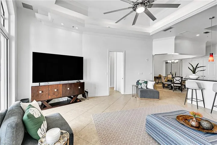 Living room featuring a raised ceiling, light tile patterned floors, a towering ceiling, ornamental molding, and ceiling fan