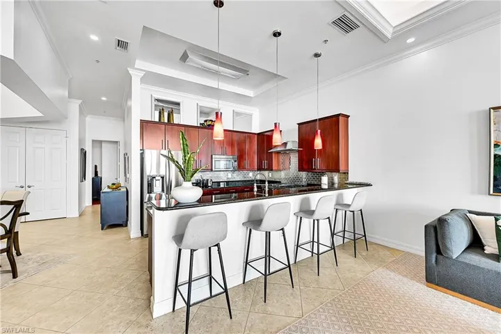 Kitchen featuring wall chimney range hood, dark brown cabinets, stainless steel appliances, dark countertops, and ornamental molding