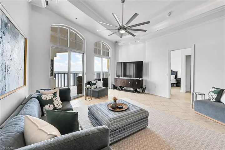 Tiled living area featuring ornamental molding, a ceiling fan, a towering ceiling, a tray ceiling, and baseboards