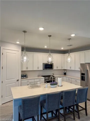 Kitchen with a kitchen bar, light wood-style floors, white cabinets, appliances with stainless steel finishes, and decorative light fixtures