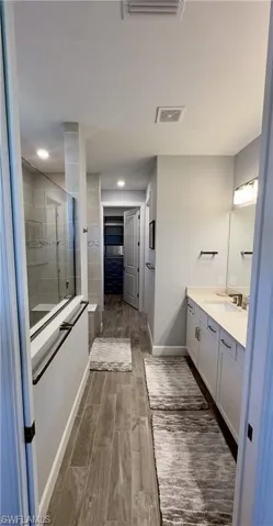 Bathroom with a spacious closet, a tile shower, vanity, wood tiled floors, and recessed lighting