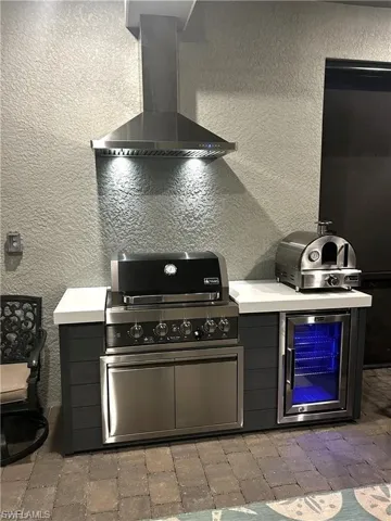 Kitchen with a textured wall, wall chimney range hood, light countertops, and beverage cooler
