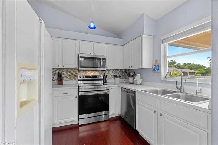 Kitchen featuring appliances with stainless steel finishes, a sink, lofted ceiling, dark wood-style flooring, and tasteful backsplash
