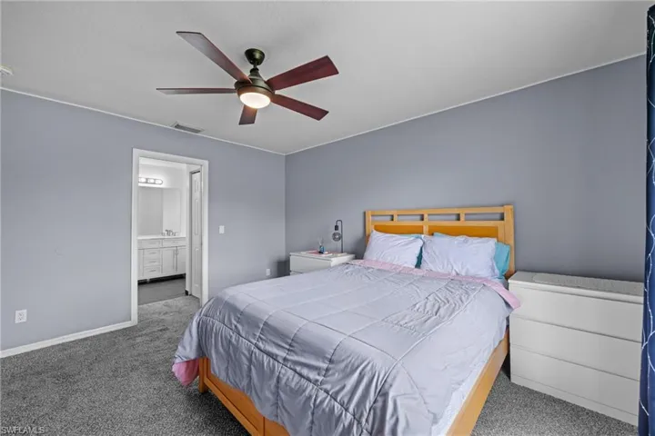Carpeted bedroom featuring ensuite bathroom, baseboards, and ceiling fan