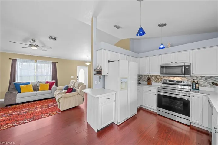 Kitchen with stainless steel appliances, lofted ceiling, open floor plan, dark wood finished floors, and decorative backsplash