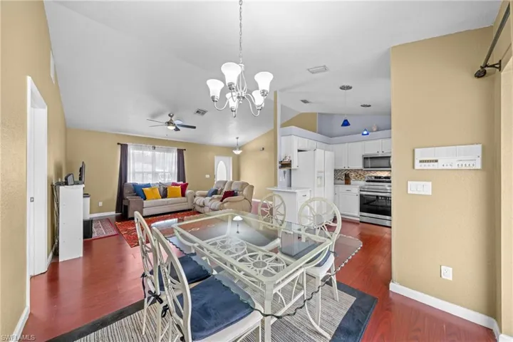 Dining area featuring lofted ceiling, a chandelier, ceiling fan, dark wood-style flooring, and baseboards