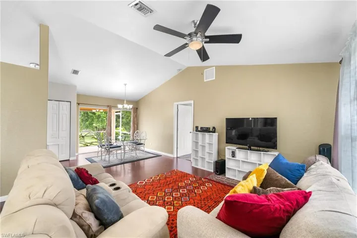 Living area featuring vaulted ceiling, a ceiling fan, baseboards, wood finished floors, and a chandelier