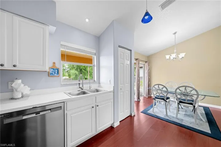 Kitchen featuring dishwasher, a sink, dark wood-type flooring, a chandelier, and white cabinets