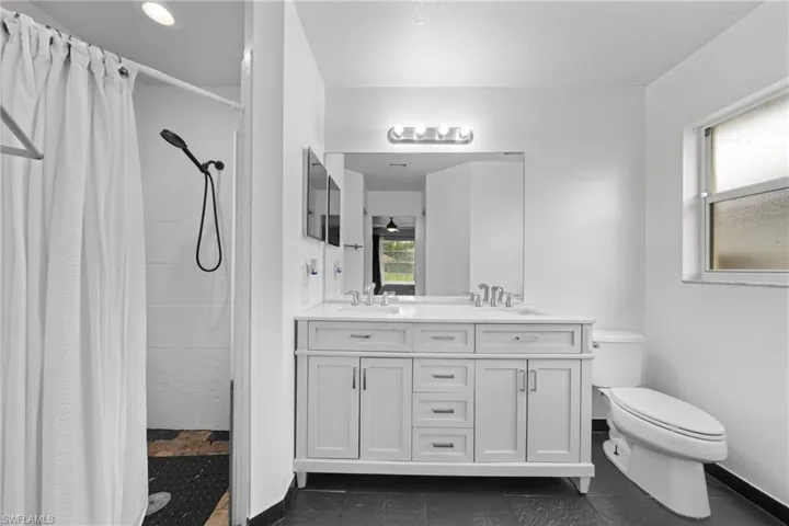 Full bathroom featuring toilet, a tile shower, double vanity, and baseboards