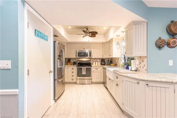 Kitchen with a raised ceiling, ceiling fan, tasteful backsplash, decorative light fixtures, and stainless steel appliances