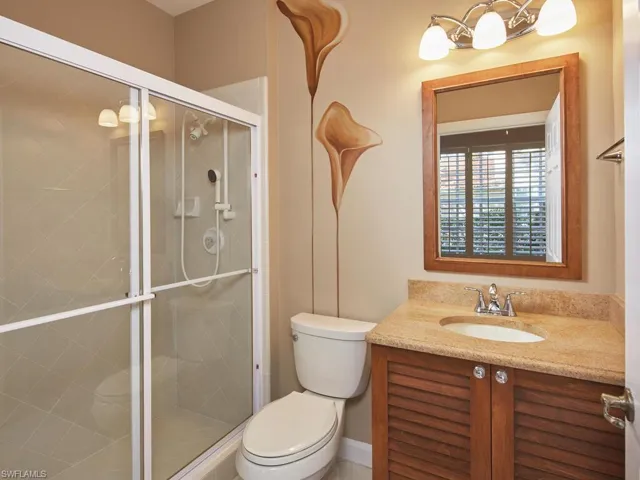 Inviting guest bathroom with tiled shower and a lovely wooden vanity with a natural stone countertop.