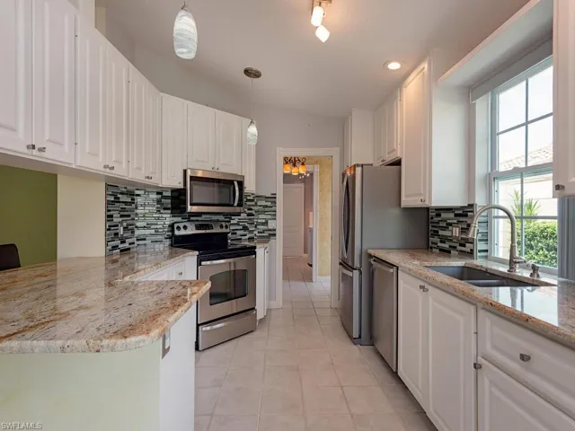 Kitchen with white cabinetry, stainless steel appliances, light stone countertops, decorative backsplash, and recessed lighting
