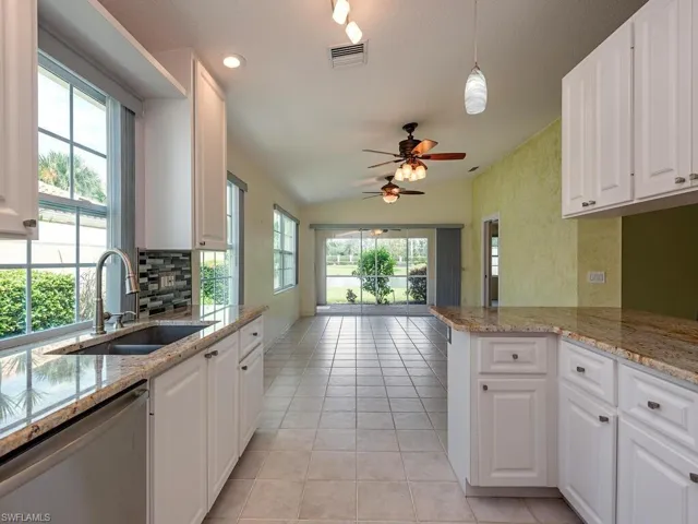 Kitchen with white cabinets, light stone counters, stainless steel dishwasher, light tile patterned floors, and lofted ceiling