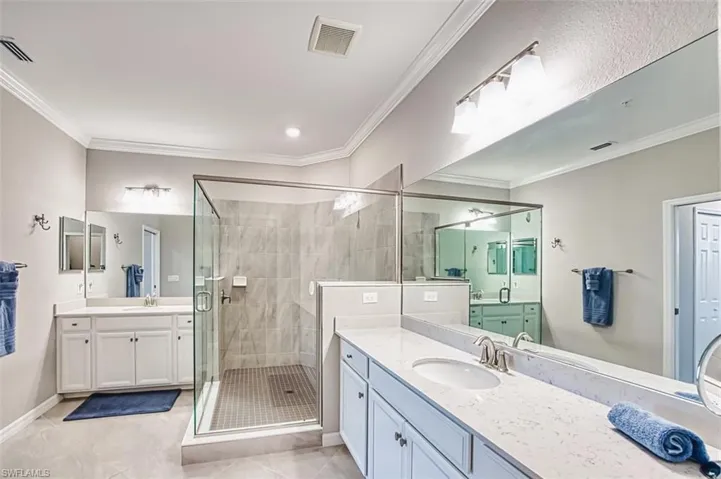 Full bathroom with light tile patterned flooring, crown molding, a shower stall, two vanities, and recessed lighting