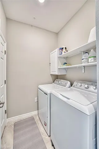 Laundry area featuring light tile patterned floors, separate washer and dryer, and cabinet space