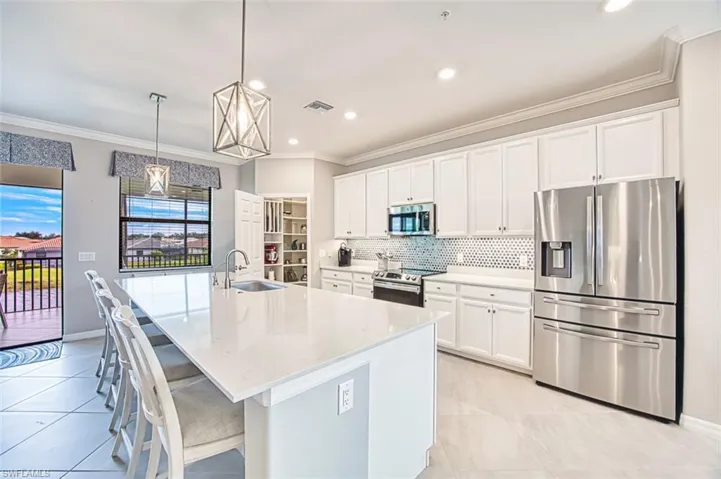 Kitchen with appliances with stainless steel finishes, crown molding, white 42"cabinets, decorative light fixtures, and backsplash