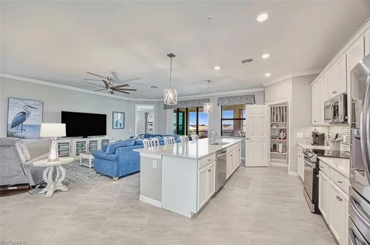 Kitchen featuring white cabinets, appliances with stainless steel finishes, ornamental molding, open floor plan, and decorative light fixtures