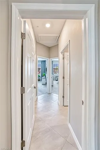Hallway with attic access and light tile patterned floors to 2 bedrooms, guest bath, and laundry room