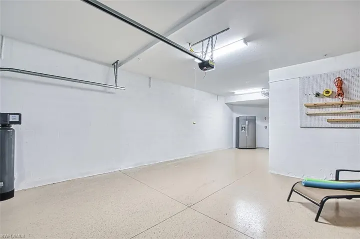 Garage with concrete block wall, stainless steel fridge, and a garage door opener