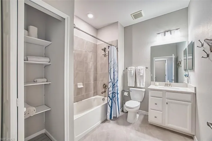Full guest bathroom with shower / bath combo with shower curtain, vanity, light tile patterned flooring, and a textured wall