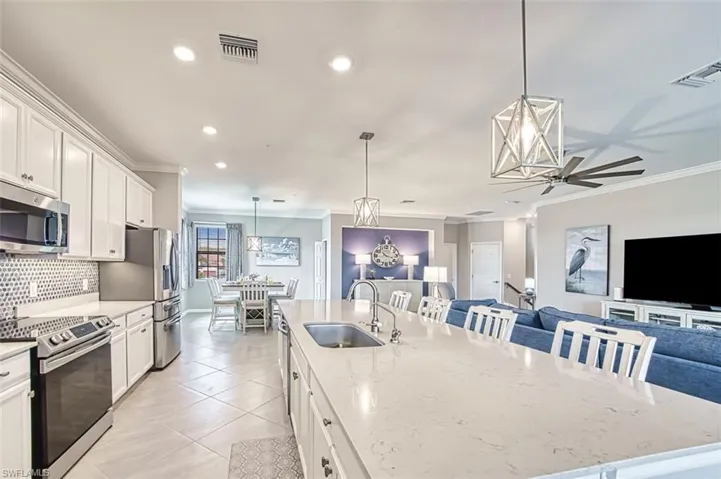 Kitchen featuring stainless steel appliances, white cabinets, hanging light fixtures, crown molding, and open floor plan large island