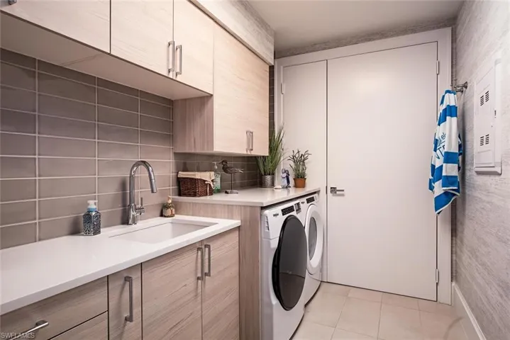 Laundry room featuring cabinets, designer wallpaper, linen closet, sliding privacy door, built-in ironing board,  separate washer and dryer, and sink