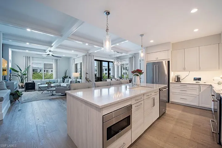 Kitchen featuring light hardwood / wood-style flooring, an island with sink, stainless steel appliances, beamed ceiling, and coffered ceiling