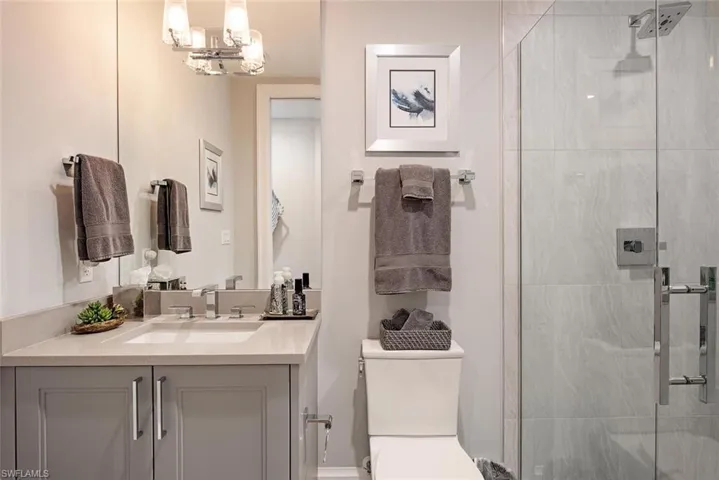 Bathroom with an inviting chandelier, an enclosed shower, vanity, and toilet