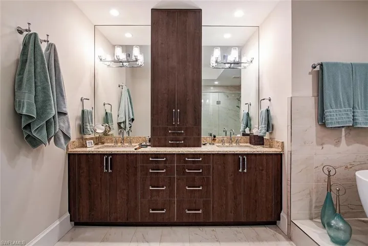Bathroom featuring tile walls, vanity with extensive cabinet space, with hidden electric receptacles, dual sinks, tile floors, and independent shower and bath