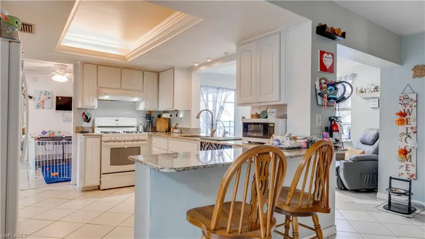 Kitchen featuring gas range gas stove, light stone counters, freestanding refrigerator, light tile patterned floors, and stainless steel microwave