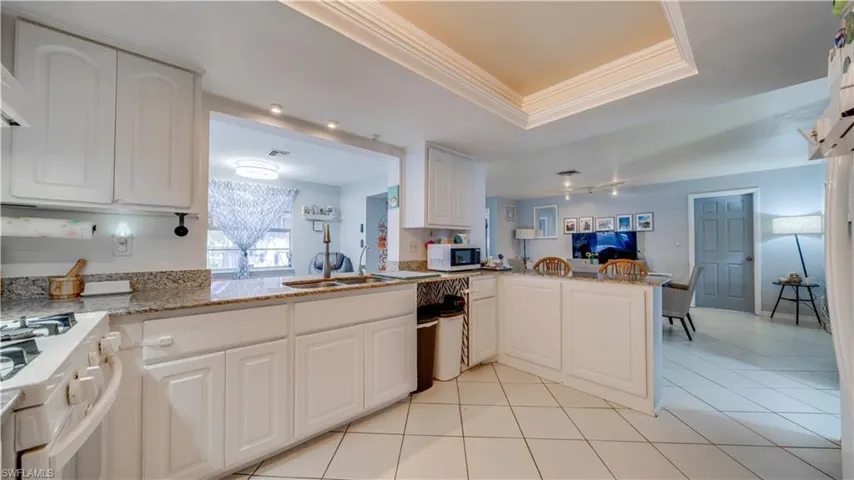 Kitchen featuring white appliances, light stone counters, white cabinetry, a raised ceiling, and crown molding