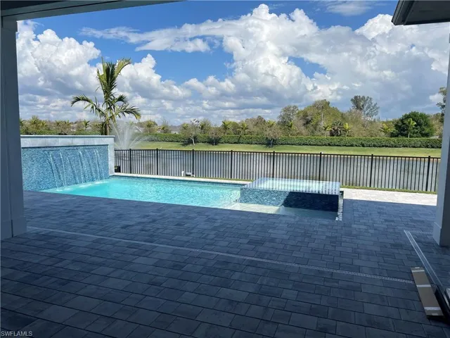 Relaxing pool / spa with a patio area, view of wooded area, a water view, and a fenced backyard