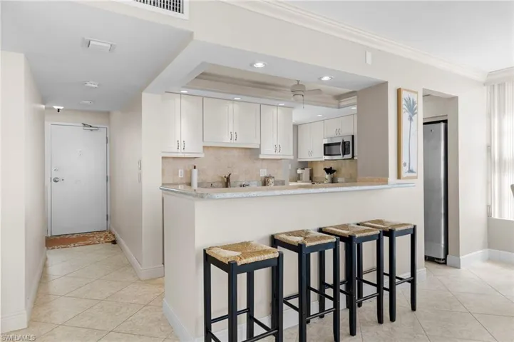 Kitchen with appliances with stainless steel finishes, white cabinets, a kitchen breakfast bar, backsplash, and ornamental molding