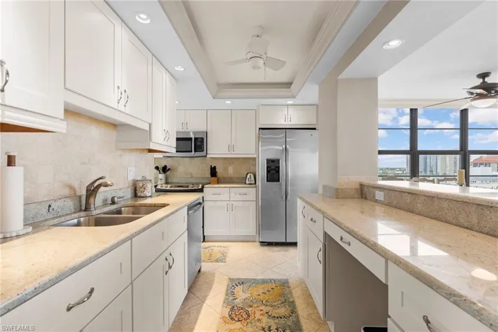 Kitchen with ceiling fan, a raised ceiling, appliances with stainless steel finishes, crown molding, and sink