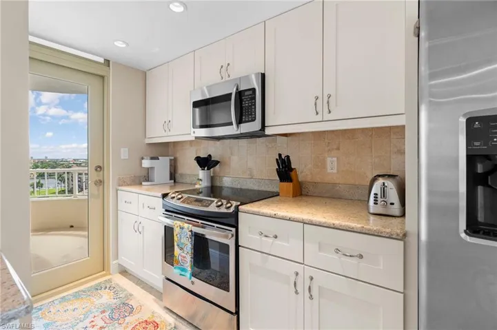 Kitchen with appliances with stainless steel finishes, tasteful backsplash, white cabinets, and light stone countertops