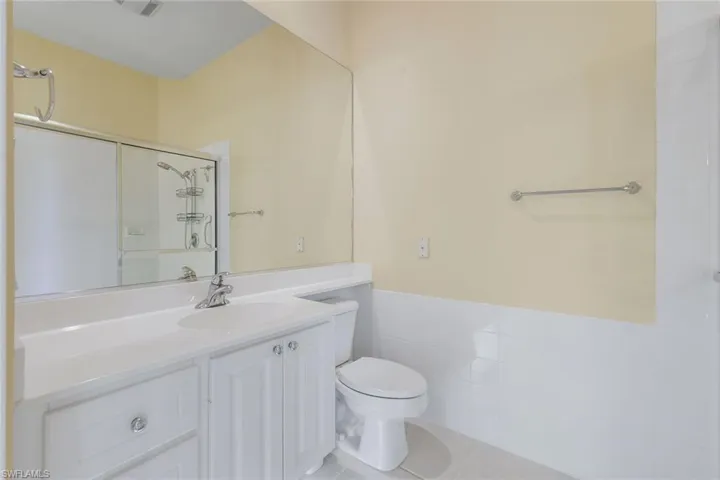Bathroom with a shower with door, toilet, vanity, tile patterned floors, and wainscoting
