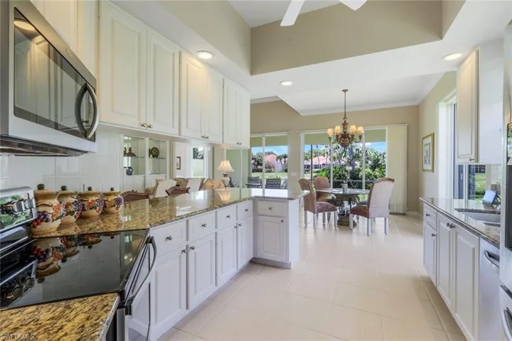 Kitchen featuring stainless steel microwave, range with electric cooktop, a chandelier, pendant lighting, and stone counters
