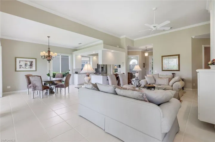 Living room with light tile patterned floors, ornamental molding, ceiling fan, a chandelier, and baseboards