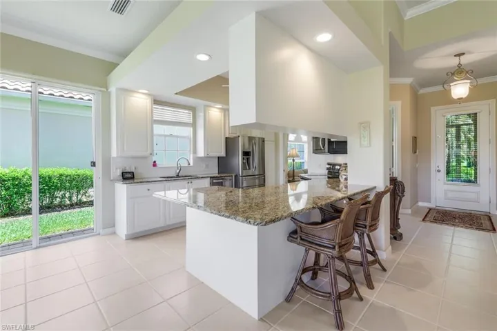 Kitchen with appliances with stainless steel finishes, a sink, ornamental molding, light tile patterned floors, and light stone counters