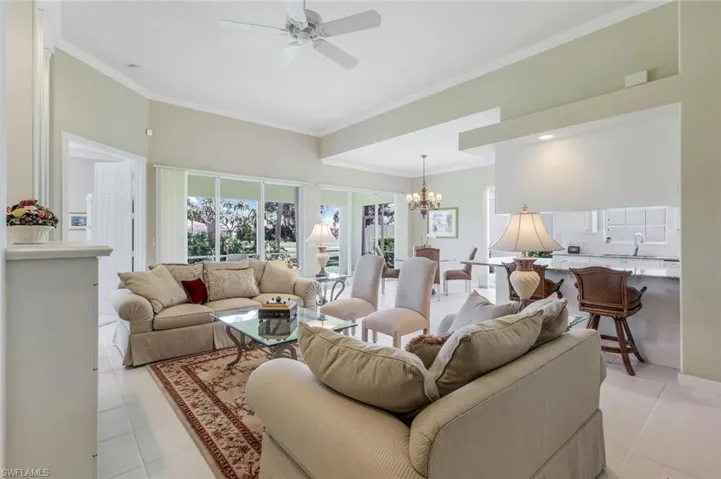 Living room featuring a ceiling fan, ornamental molding, light tile patterned floors, and a chandelier