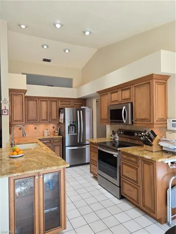Kitchen featuring lofted ceiling, sink, light stone counters, kitchen peninsula, and stainless steel appliances