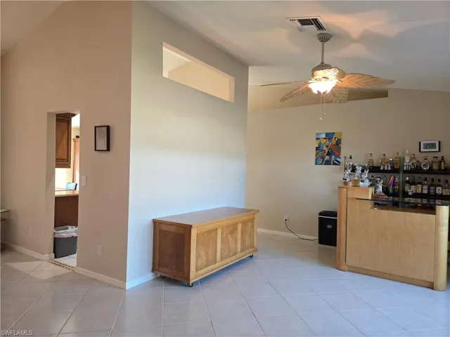 Bar with ceiling fan, light tile patterned floors, light brown cabinetry, and lofted ceiling