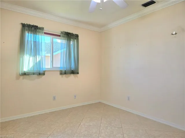 Empty room featuring ceiling fan, light tile patterned flooring, and ornamental molding