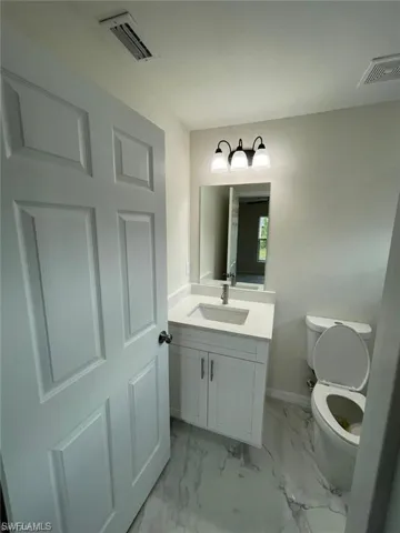 Half bathroom featuring vanity, toilet, baseboards, and marble look tiles