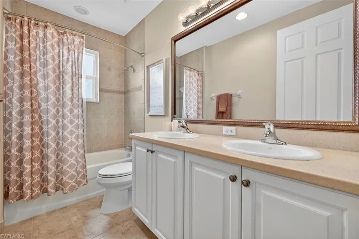 Bathroom featuring shower / bath combination with curtain, double vanity, and light tile patterned floors