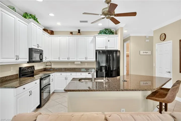 Kitchen with black appliances, white cabinets, ornamental molding, light tile patterned floors, and dark stone countertops