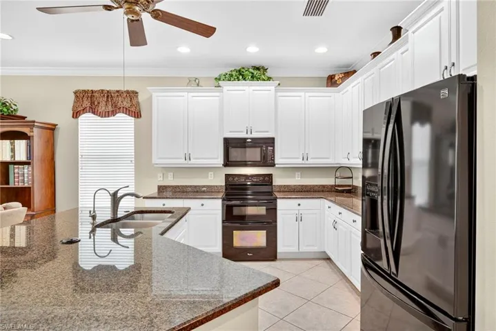 Kitchen with black appliances, white cabinets, light tile patterned floors, dark stone counters, and crown molding
