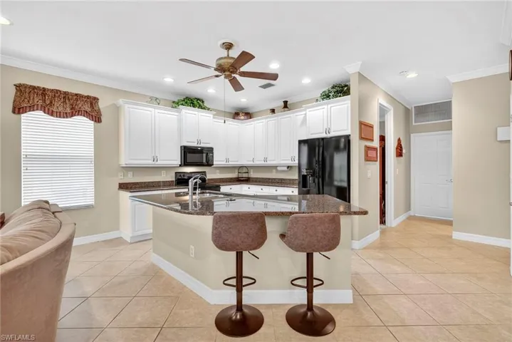 Kitchen featuring crown molding, light tile patterned floors, a kitchen island with sink, white cabinets, and dark stone countertops