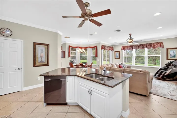 Kitchen with light tile patterned floors, white cabinets, dark stone countertops, ornamental molding, and open floor plan